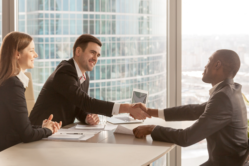 Global Mobility Solutions - Benefits of Tiered Relocation Policies One woman and two men in office, all dressed in business attire, shaking hands after submitting a Request for Proposal