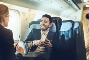 businessman on plane smiling while speaking to other passengers
