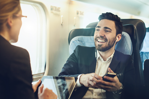 Businessman using travel tools for corporate relocation from Global Mobility Solutions Handsome man with brown hair, mustache, and beard, riding in car, phone to ear, laptop open, smiling, talking about his company’s Critical Questions