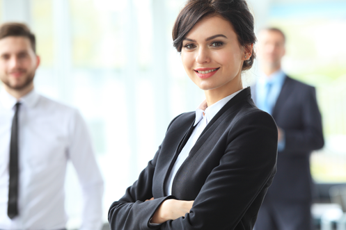 Woman executive with short brown hair and business suit smiling, co-workers behind her, all benefitting from technology trends that allow for global talent mobility
