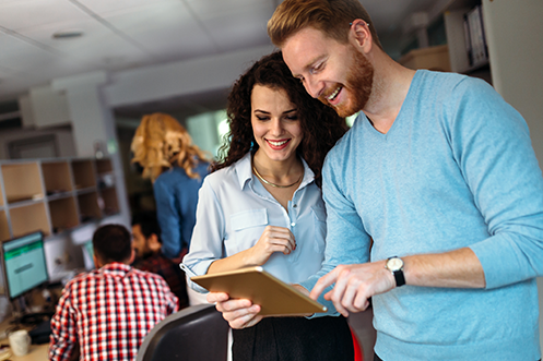 Woman with dark hair in white shirt, handsome man with red hair and beard in blue shirt, looking at a tablet and participating in some of the USA’s fastest growing jobs