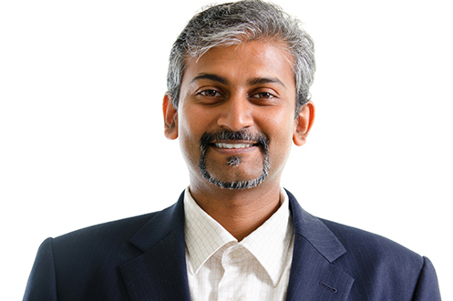 Handsome India businessman with black and gray hair, mustache and goatee, facing front, smiling, wearing a white shirt and blue jacket, grateful for ruling by India’s Supreme Court