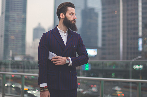 Handsome man with dark hair and long beard, holding a Chinese newspaper in his arm, wearing dark jacket, contemplating China residency rules as they impact his tax obligations.