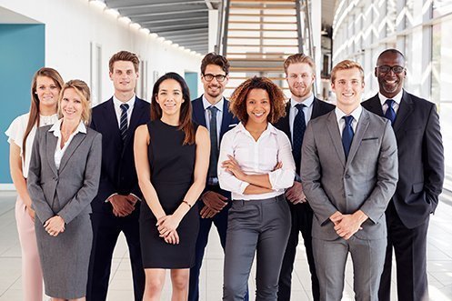 Four women and five men, employees in business attire, smiling in the lobby of an office building, thinking about how BREXIT impacts their job searches