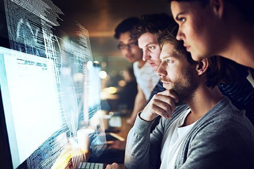 Three male computer programmers and one female computer programmer, central male figure has beard, all four are looking at a computer screen with programming code while they use cloud computing