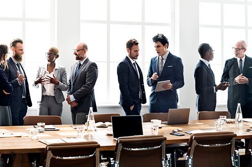 Group of nine business people comprising three women and six men, all of various ages, races, cultures, and identities, discussing the benefits of diversity and inclusion initiatives