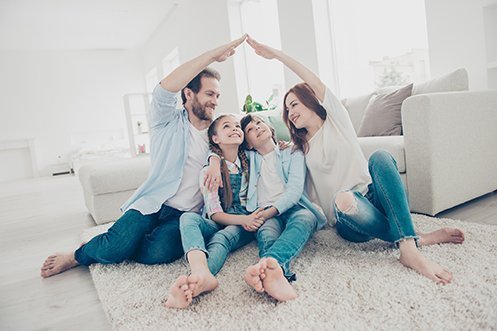 Handsome man in blue shirt and jeans, brown hair, beard, smiling, woman in white shirt and jeans, long red hair, smiling, both reaching over to touch their hands in a roof format over their two children in their new house they purchased using new real estate business models