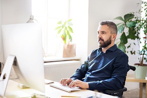Businessman in wheelchair at his desk, wearing blue shirt, with a full beard and mustache, smiling, choosing relocation technology