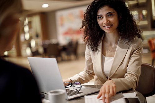 Woman with curly hair, white shirt, and tan jacket, facing forward, smiling, working with her expense management program