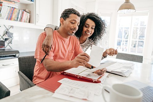 Man in orange shirt and woman in black and white striped shirt, married couple, both working, looking at a project together, benefitting from employment assistance for spouses which was encourage in the 2019 Corporate Relocation Survey