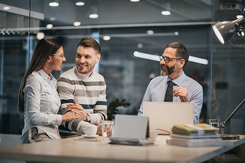 Woman with long dark hair wearing glasses and white shirt, smiling, holding arm of man with short hair, beard and mustache, wearing a striped sweater, smiling, with man to the right wearing glasses, with full beard, wearing shirt and tie, RealtorĀ® asks relocating employees questions about their coming move