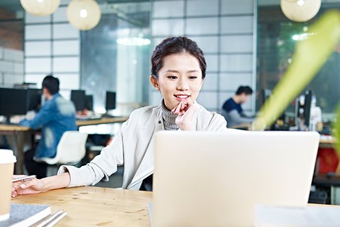 Woman with dark hair, smiling, looking at computer, searching for Singapore tech talent