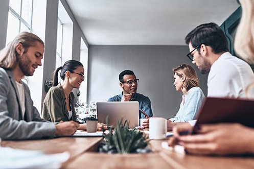 Three men and three women, one woman is partially out of the image, working as a project team around a table to determine the company’s year-end relocation expense reconciliation