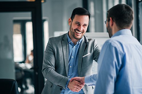 Two men shaking hands, smiling at each other, both with dark hair and beards, talking about the benefits of affinity programs