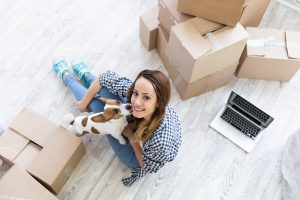 young woman with friendly dog in their new house with moving boxes.