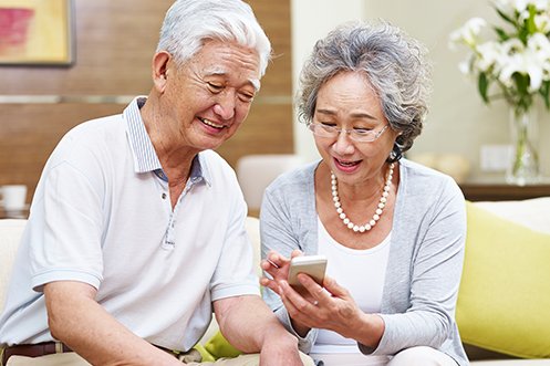 Older Japanese man and woman smiling, looking at phone, discussing how aging impacts country demographics