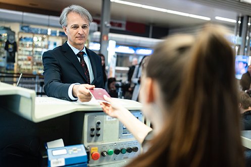 Male business traveler wearing a suit and tie with white shirt, handing his passport and documents to a border control agent during an emergency repatriation