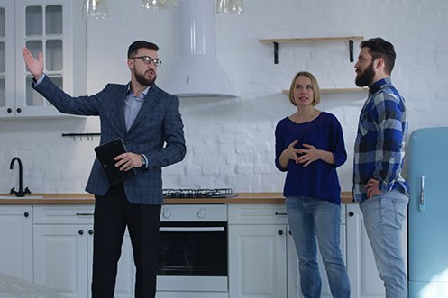Man with beard and dark hair, licensed professional appraiser with glasses and blue jacket, talking to two homeowners, a woman in blue shirt with blonde hair and a man in blue check shirt with dark hair and beard, about their home relocation appraisal
