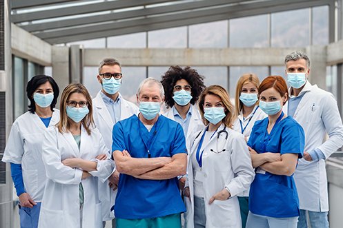 Group of nine healthcare workers, five women and four men, all wearing masks and facing forward, benefitting from healthcare corporate housing solutions
