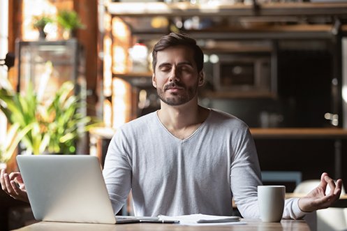 Businessman with beard, mustache, facing a computer, in Zen position, calm, eyes closed, practicing good mental health