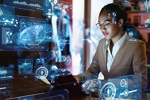 Female engineer working on computer with graphics, wearing glasses and tan coat, employer had to pay higher immigration application fees to bring her to the US