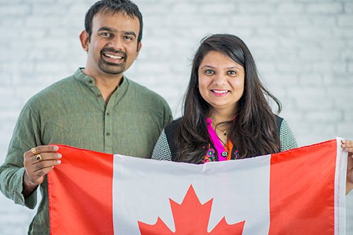 India man and woman, both foreign nationals, facing forward, smiling, holding up a Canadian flag, hired by a US employer under Canada immigration alternatives