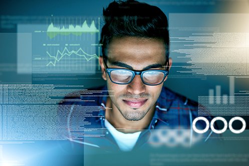 Male information technology programmer wearing glasses, facing down at a computer screen and smiling, with dark hair, benefiting from the 2020 H-1B Visa Program
