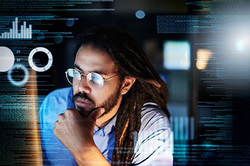 Man wearing round eyeglasses, long dark hair, wearing a blue shirt, looking at a computer screen as he works on programming for a relocation integration