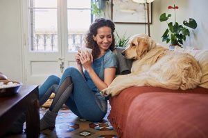 Woman sitting on floor, smiling, holding coffee cup, looking at large dog in in their temporary housing