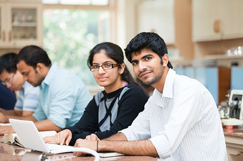 Female student with long dark hair, wearing glasses, smiling, and male student with shorter dark hair, mustache and beard, wearing white shirt, both from India, both came into the US during 2020 inbound immigration to learn and obtain job under a class of visas