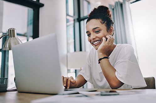 Woman smiling, looking at laptop, wearing white shirt, with dark hair, submitting remote worker expenses online through an expense management program