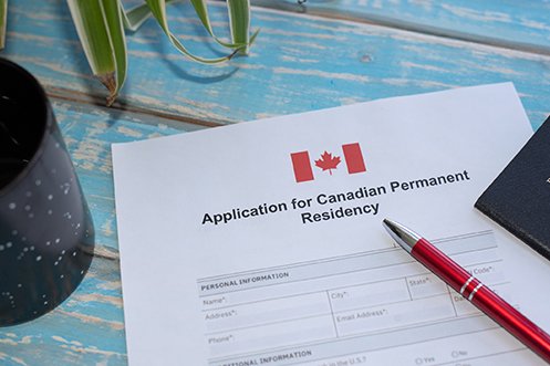 Canada citizenship path expanding and will allow temporary residents to more easily apply for permanent residency with the application shown on a table, with a pen ready for filling out the paperwork