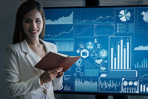 Business woman with long dark hair, wearing a light-color business jacket, holding a book, smiling in front of a data display showing industry-leading relocation technology