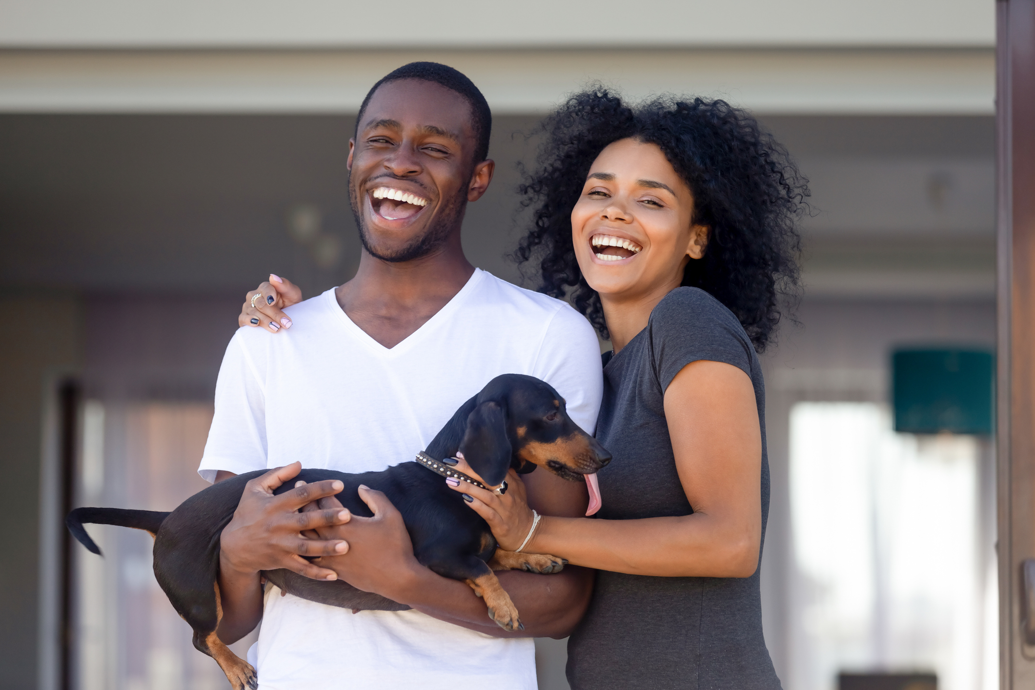young couple holding puppy in front of their new house