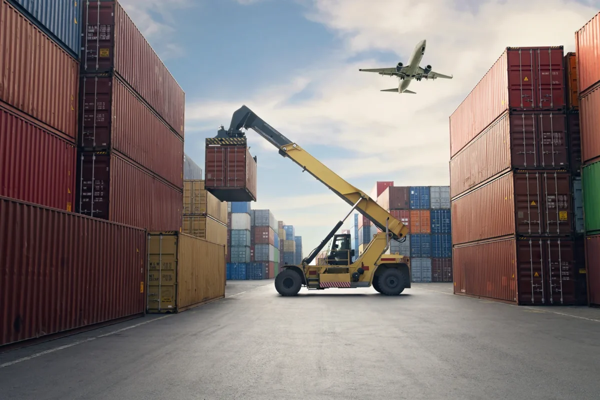 airplane flying over large shipping containers