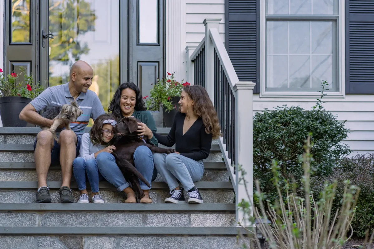 happy family sitting on front steps of home petting their dogs